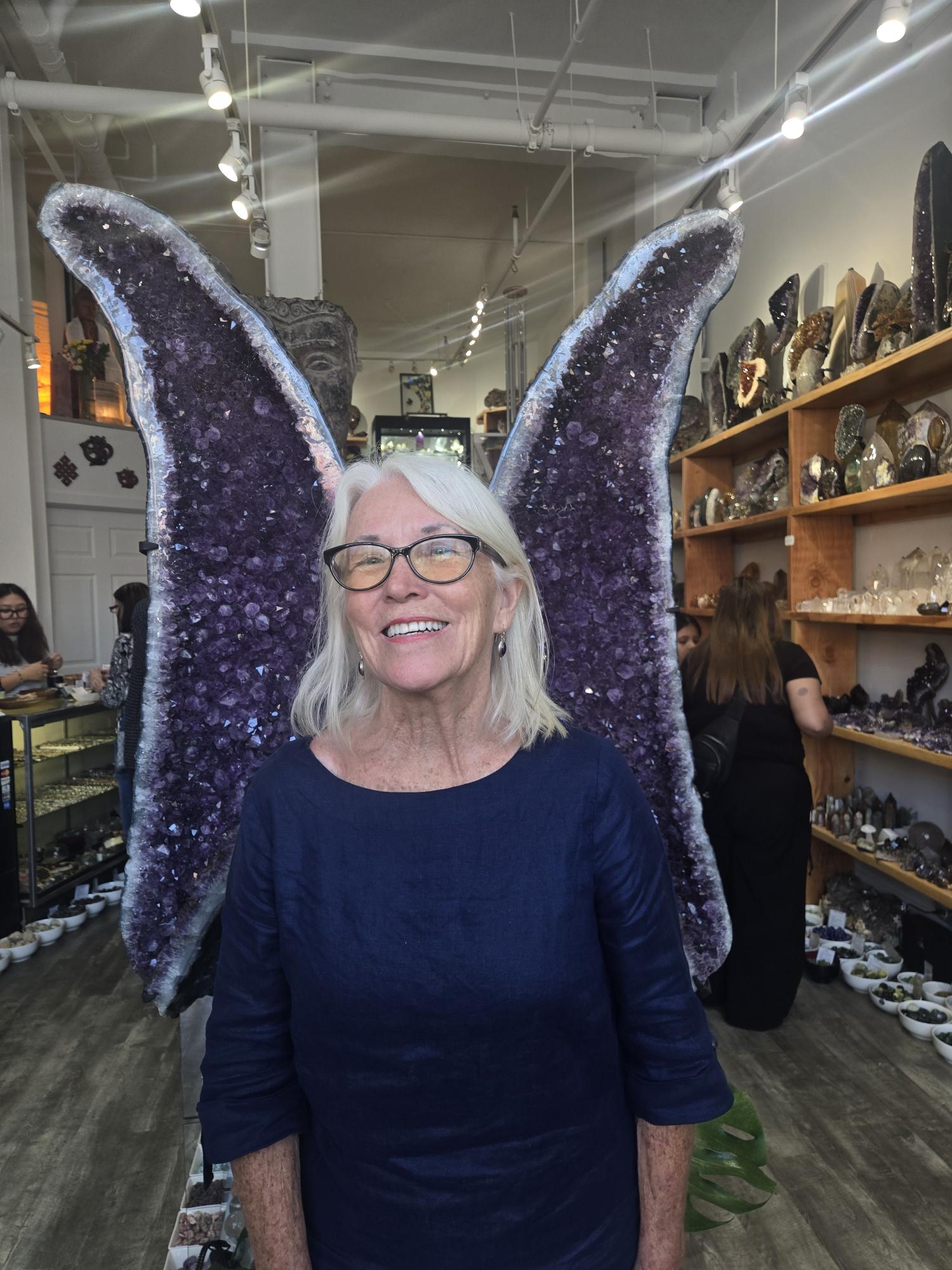 A guest beaming in front of a giant amethyst geode shaped like butterfly wings during a Sticks and Stones crystal tour